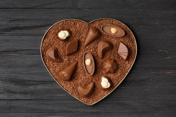 Chocolate candies in chocolate chips in a heart-shaped box on a dark wooden background top view, Valentine\'s Day.