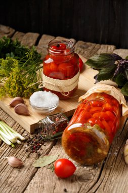 Kapalı ve açık bir kavanozda vişneli domates turşusu, sarımsak, yeşil soğan, dereotu, fesleğen ve baharat eski ahşap arka planda. Ev yapımı konserve domates ve terbiye malzemeleri..