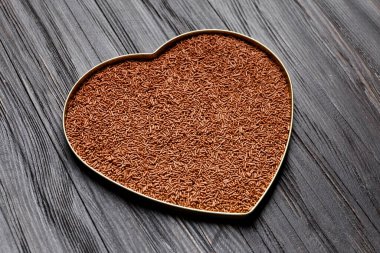 Koyu ahşap arka planda kalp şeklinde bir kutuda çikolata parçacıkları..