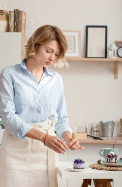 Mutfakta genç bir kız doğum gününde kek için mum yakıyor. Yalnız bir kız kendine tatil yapar. Önlüklü mutlu kız mutfakta mum yakıyor.