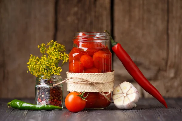 stock image Pickled cherry tomatoes in an open glass jar, chili peppers, garlic, seasonings, spices and herbs for marinade close-up on a dark wooden background. Home preservation.