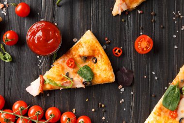 Kurutulmuş, zeytinli, peynirli ve otlu pizza dilimleri koyu ahşap arka planda, taze vişneli domates, sos ve pizza üst görünümü için baharatlarla servis edilir. İtalyan yemeği..