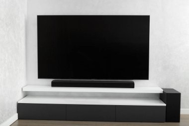 Oturma odasının içinde duvarında televizyon, hifi ekipmanları, ses çubuğu, gri dolap olan bir yer. Televizyon ve müzik sistemi iç kısımda. Parlak renklerle modern oturma odası.