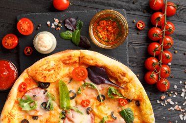Kurutulmuş et, zeytin, peynir ve otlu pizza siyah taş tabakta, soslar, baharatlar, koyu ahşap arka planda taze sebzeler, üst manzara. Geleneksel İtalyan yemekleri.