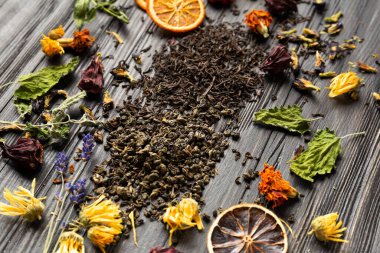 Kuru siyah ve yeşil çay, kurutulmuş narenciye dilimleri, nane yaprakları ve kuru amber çiçeği, takviye, lavanta çiçekleri yakın plan koyu ahşap arka plan görüntüsü.