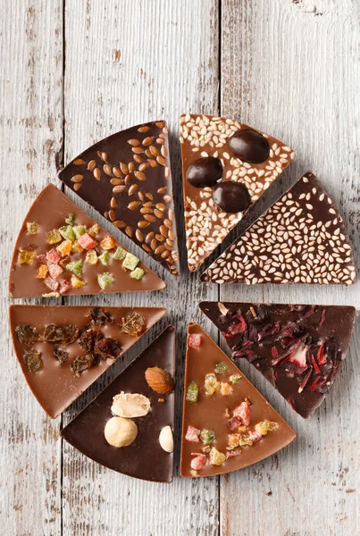 Creative composition chocolate in the shape of a pizza with candied fruits, nuts, dry berries, chocolate pizza and ingredients on a wooden background.