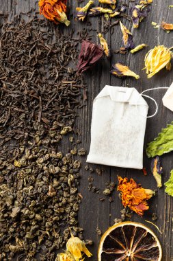 Kuru siyah ve yeşil çay, çay poşeti, kurutulmuş narenciye dilimleri ve koyu ahşap arka plan manzaralı kuru amber çiçekleri. Koyu arkaplanda farklı türde kuru çay..