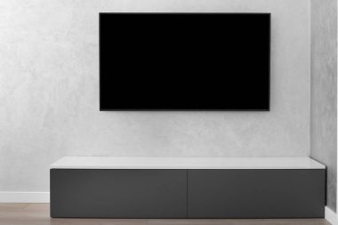 Modern bir oturma odasının bir parçası, gri bir duvarda akıllı bir LED TV, gri bir dolap, bir halı. İç mekanda minimalizm. Hafif tonlu oturma odaları.