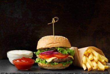 Lezzetli iştah açıcı sığır burger, patates kızartması, siyah arka planda siyah bir tabakta iki sos. Amerikan fast food, ev yapımı hamburger..