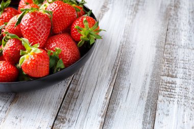 Hafif ahşap zemin üzerinde siyah yuvarlak bir tabakta taze organik çilekler, metin için yer var..