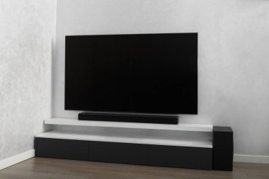 Oturma odasının içinde duvarında televizyon, hifi ekipmanları, ses çubuğu, gri dolap olan bir yer. Televizyon ve müzik sistemi iç kısımda. Parlak renklerle modern oturma odası.