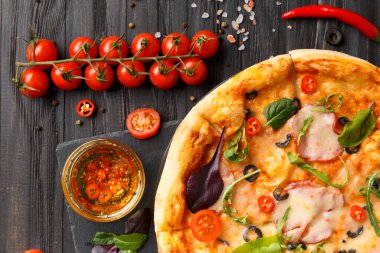 Kurutulmuş et, zeytin, peynir ve otlu pizza siyah taş tabakta, soslar, baharatlar, koyu ahşap arka planda taze sebzeler, üst manzara. Geleneksel İtalyan yemekleri.