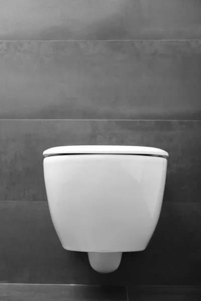 閉じられた蓋と黒い壁に対する光沢のあるクロムフラッシュボタンを備えたモダンな壁に取り付けられた白いトイレ 浴室の奥にある便器 — ストック写真