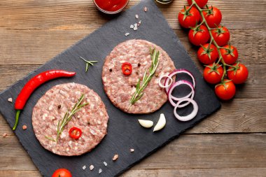 Çiğ kıymalı burger köfteleri, biberiye, sebze ve baharatlar tahta arka planda siyah bir taş tabakta, üst manzara. Hamburger için malzemeler..