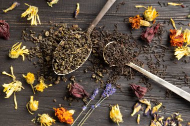 Antika kaşıklar, kuru amber çiçeği, lavanta çiçekleri ve koyu ahşap arka plan manzaralı koyu siyah ve yeşil çay karışımı. Koyu arkaplanda farklı türde kuru çay..