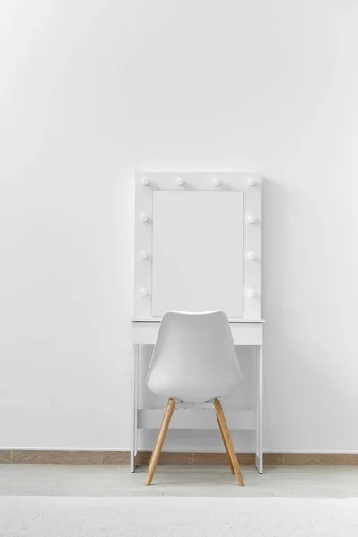 White dressing table for make-up with a large mirror and lamps, a white chair against the background of the wall. Makeup artist workplace, modern dressing room.