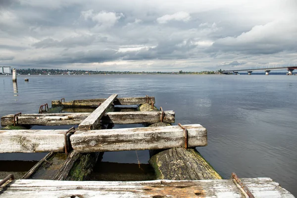 stock image Old wooden pier on the river overlooking the city. A small destroyed bridge in the water.