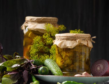 Pickled cucumbers in a jar, canned sliced cucumber salad, fresh gherkins, herbs and spices on a dark background, close-up.