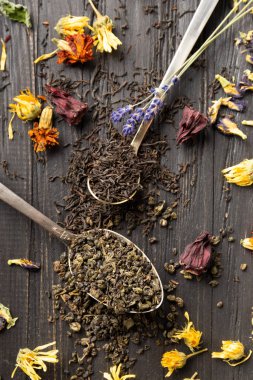 Antika kaşıklar, kuru amber çiçeği, lavanta çiçekleri ve koyu ahşap arka plan manzaralı koyu siyah ve yeşil çay karışımı. Koyu arkaplanda farklı türde kuru çay..