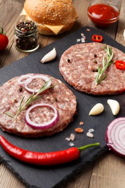 Çiğ kıymalı burger köfteleri, biberiye, sebze ve baharatlar ahşap bir arka planda siyah bir taş tabakta. Hamburger için malzemeler..
