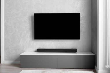 Oturma odasının içinde duvarında televizyon, hifi ekipmanları, ses çubuğu, gri dolap olan bir yer. TV ve müzik sistemi iç mekanda.