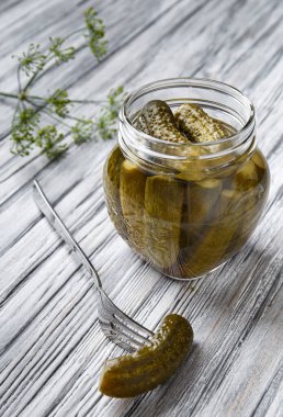 Açık kavanozda ev yapımı salatalık konservesi, çataldaki bir turşu gri dokuya yakın bir yerde duruyor. Salatalık turşusu, konserve sebze.