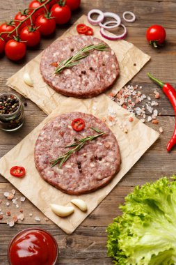 Baharatlı hamburgerler ve parşömen, sos, taze sebze, ahşap zeminde hamburgerler..