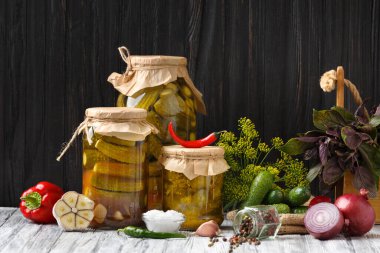 Pickled cucumbers in a jar, canned sliced cucumber salad, fresh gherkins, herbs and spices on a dark background, close-up.