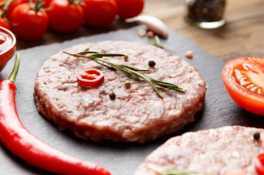 Çiğ kıymalı burger köfteleri, biberiye, sebze ve baharatlar ahşap bir arka planda siyah bir taş tabakta. Hamburger için malzemeler..