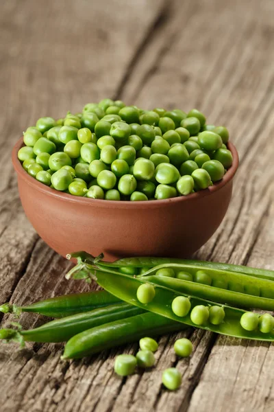 Peeled green peas in a clay bowl, sweet organic green peas in closed and open pods and scattered grains on an aged wooden background. vegetable protein.