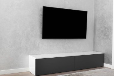 Modern bir oturma odasının bir parçası, gri bir duvarda akıllı bir LED TV, gri bir dolap, bir halı. İç mekanda minimalizm. Hafif tonlu oturma odaları.