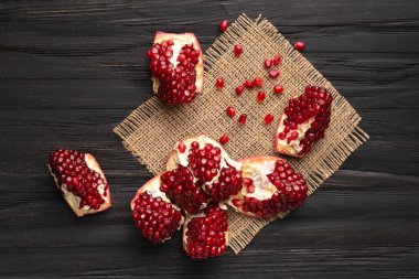 Olgun, büyük, sulu çekirdekli büyük bir nar, ahşap bir arka planda parçalara ayrılır. Üst manzara, nar taneleri etrafa saçılır..