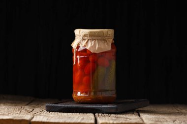 Kavanozda çeşitli kiraz domatesleri ve salatalıklar var. Koyu bir arka planda el işi kapağı, yazı için yer var. Terbiye edilmiş sebze.