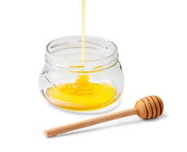 Honey is poured into an empty glass transparent jar and a wooden dipper on a white background close-up. Organic honey flows into a bowl on isolation. Pouring honey macro photography