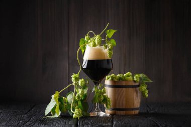 Bir bardak koyu bira, zıpzıp dalları ve ahşap zıplı tahta bir fıçı. Bira gelenekleri. Oktoberfest. Bira festivali. Aziz Patrick Günü.