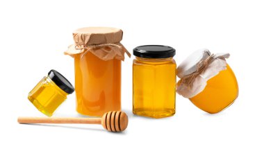 Farklı şekil ve boyutlarda bal içeren şeffaf kavanozlar yan yana durur ve beyaz arka planda ahşap kaplama bulunur. Tecrit edilmiş bal kavanozlarının kavramsal bileşimi.