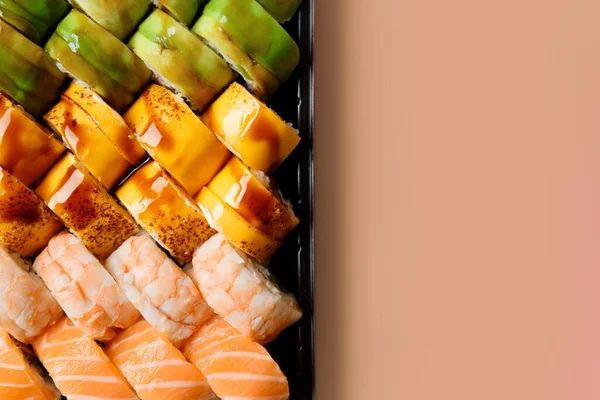 A set of bright multi-colored sushi rolls with shrimp, salmon, eel, avocado, cheese in plastic packaging, on a light background, top view, close-up, copy space. Sushi delivery