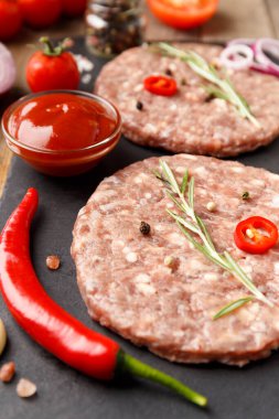 Çiğ kıymalı burger köfteleri, biberiye, sebze ve baharatlar ahşap bir arka planda siyah bir taş tabakta. Hamburger için malzemeler..