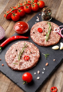 Çiğ kıymalı burger köfteleri, biberiye, sebze ve baharatlar ahşap bir arka planda siyah bir taş tabakta. Hamburger için malzemeler..