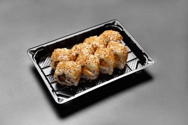 Sushi rolls with salmon in a plastic package, on a black background, top view. Delivery of sushi, rolls in a takeaway package.