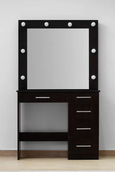 Dark makeup dressing table with a large mirror and lamps against a white wall. Makeup artist\'s workplace, modern dressing room.