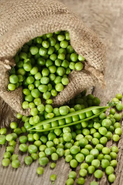 Fresh organic peeled green peas in a burlap bag, open green pea pods, scattered ripe pea seeds on an aged wooden background. Vegetable protein, healthy products.