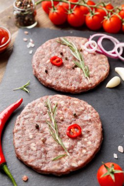 Çiğ kıymalı burger köfteleri, biberiye, sebze ve baharatlar ahşap bir arka planda siyah bir taş tabakta. Hamburger için malzemeler..