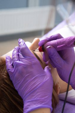 Güzellik hocası bir güzellik salonunda kalıcı kaş makyajı yapıyor, yakın plan. Bir kozmetolojistin elleri kaş mikro patinajı yapıyor. Yüzünde dövme var..