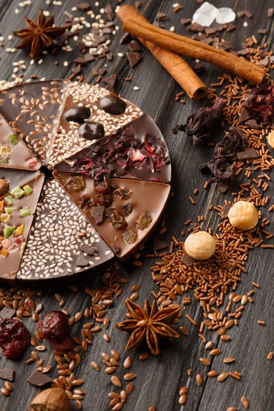 Creative composition chocolate in the shape of a pizza with candied fruits, nuts, dry berries, chocolate pizza and ingredients on a dark wooden background.