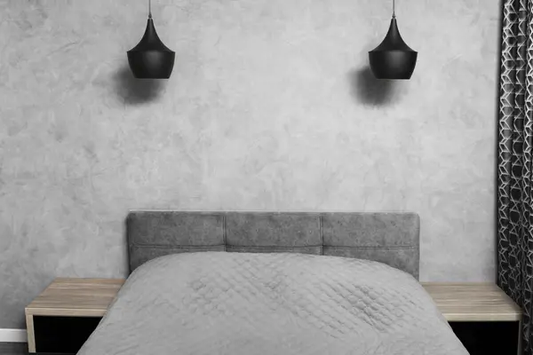 Modern design of the bedroom in gray tones, minimalism in the interior. A large bed in the bedroom, bedside tables with black glass, black chandeliers, carpet.