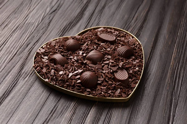 Chocolate candies in chocolate chips in a heart-shaped box on a dark wooden background top view, Valentine\'s Day.