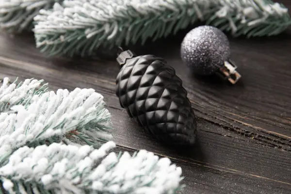 New Year\'s decor on a dark background. Fir branch in the snow and Christmas decorations in black on a wooden background.