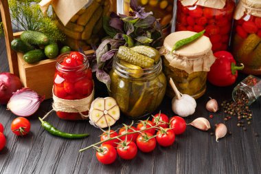 Kavanozlarda konserve kiraz domatesleri ve salatalıklar, taze sebzeler, baharatlar ve salamura için baharatlar ahşap bir arka planda. Sebze turşusu.