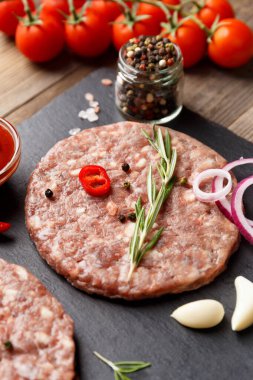 Çiğ kıymalı burger köfteleri, biberiye, sebze ve baharatlar siyah taştan bir tabakta, ahşap bir arka planda, yakın plan. Hamburger için malzemeler..